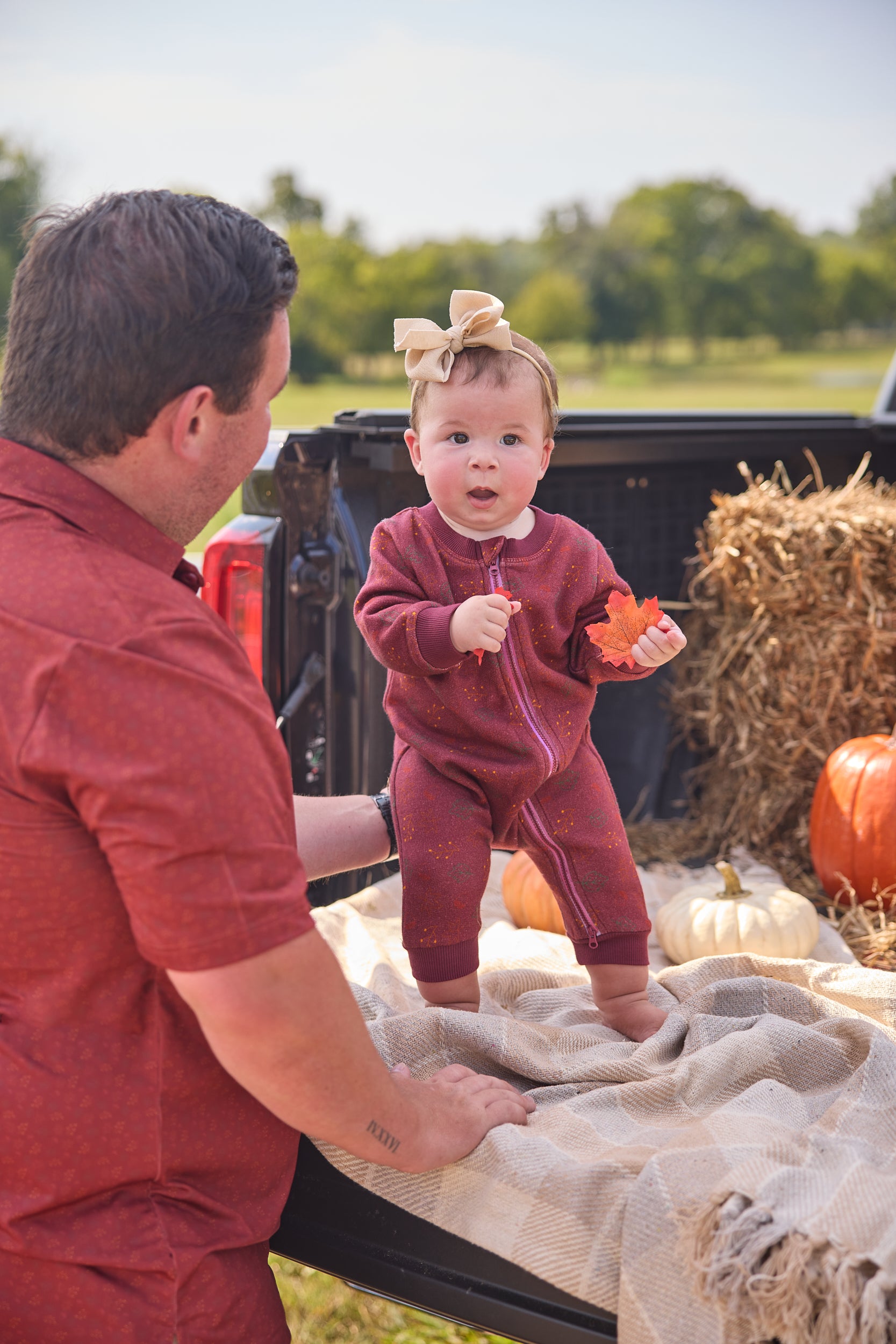 Man and young child in a pumpkin patch with hay bales and pumpkins.